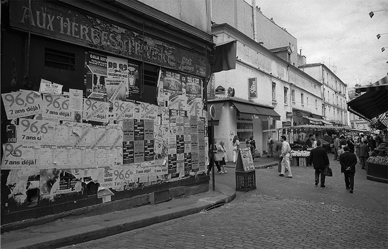 Pendant l&#039;été 1987 à Paris, un commerce voit ses façades envahies par les affiches du moment, à proximité du marché.